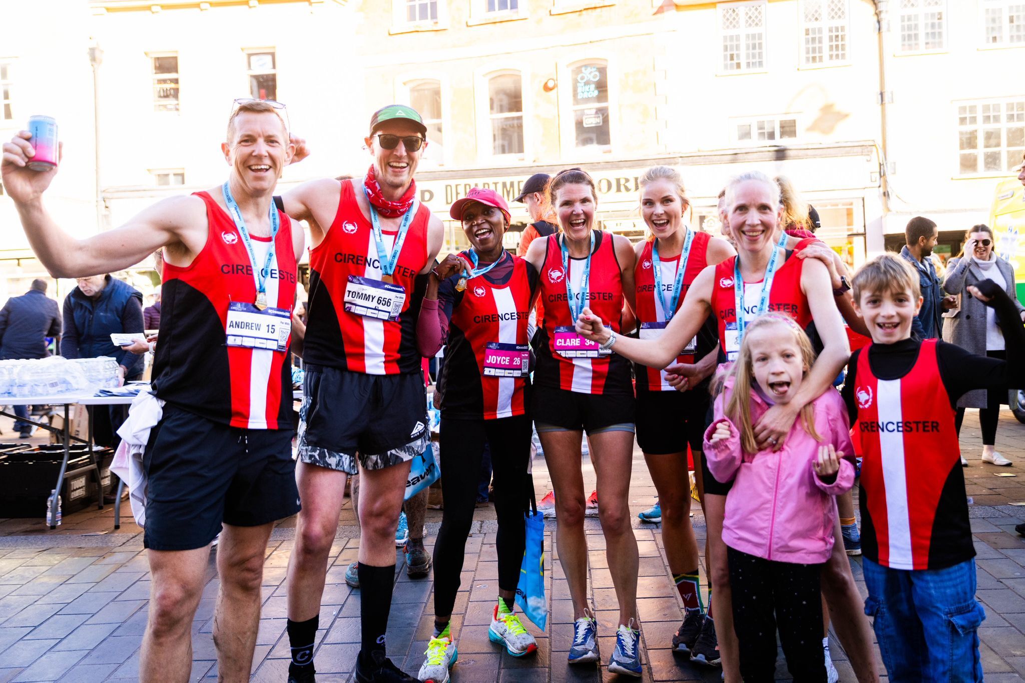 Runner nearing a marathon finish line, wearing a race bib and hydration vest. A hand holds medals in the foreground. Urban backdrop with onlookers.wearing a race bib and hydration vest. A hand holds medals in the foreground. Urban backdrop with onlookers.